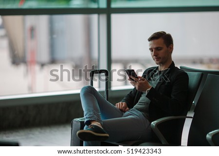 Urban business man talking on smart phone traveling inside in airport. Casual young businessman wearing suit jacket. Handsome male model. Young man with cellphone at the airport while waiting for