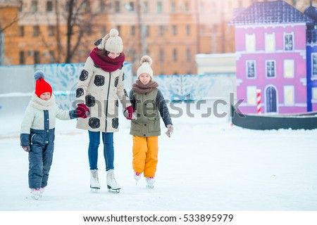 Little adorable girls with mother learning to skate on ice-rink
