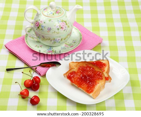 Jam toast with cherries/Jam toast/Jam toast with fresh cherries on a checked cloth with teapot in background.