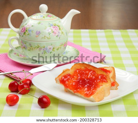 Jam toast with cherries/Jam toast/Jam toast with fresh cherries on a checked cloth with teapot and tabletop in background.