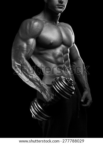 Handsome power athletic man with dumbbell. Strong bodybuilder with six pack, perfect abs, shoulders, biceps, triceps and chest. Black and white photo.