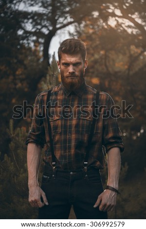 Brutal bearded man standing alone in forest outdoor with sunset nature on background