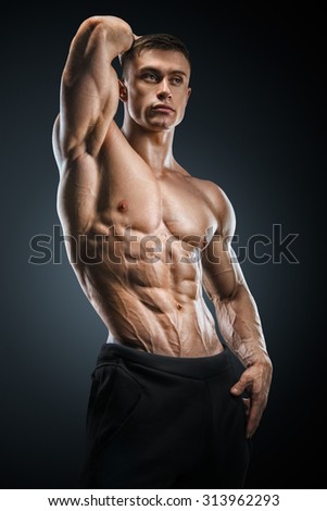 Muscular and fit young fitness male model posing over black background. Strong bodybuilder with six pack, perfect abs, shoulders, biceps, triceps and chest.