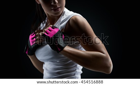 Close up portrait of female bodybuilder wearing gloves ready for gym exercise. Horizontal studio shot with copy space on black background