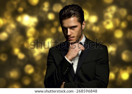 Portrait of handsome stylish man in elegant black suit golden bokeh