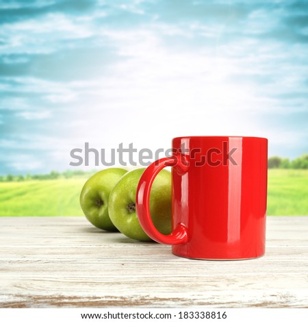 red mug apples of green and blue sky