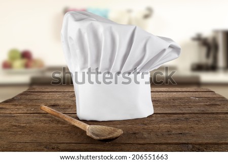 single wooden spoon and white cook hat on table of wood