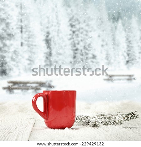 winter background of wooden old table with landscape of park in snow and mug of red