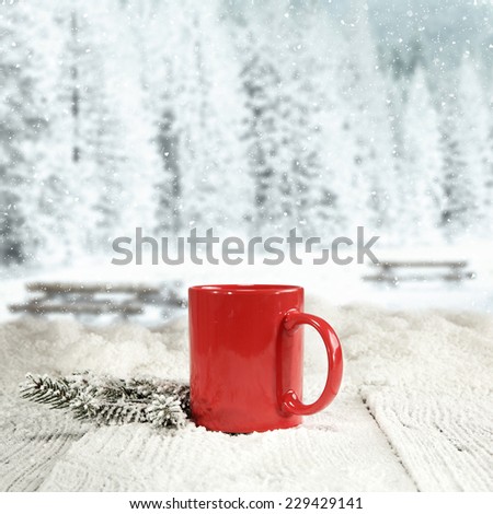 winter background of wooden old table with landscape of park in snow and red mug and green tree