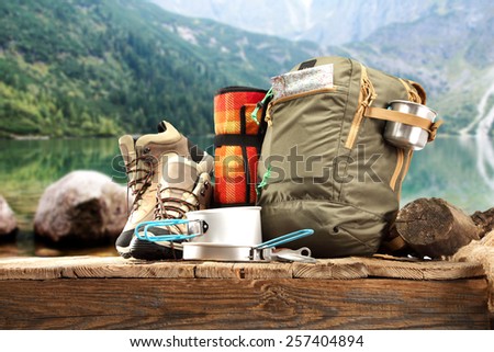 wooden pier and backpack and shoes of brown color and lake of green color at summer time