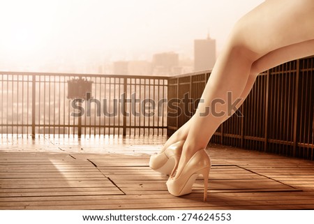 woman legs and wooden terrace with landscape of city and sunset