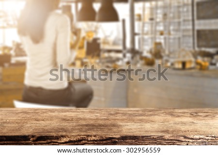 blurred background of bar with woman on chair and brown wooden desk in room of sun light
