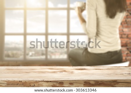 blurred background of wall of red color and white window and young woman on chair and table of wood