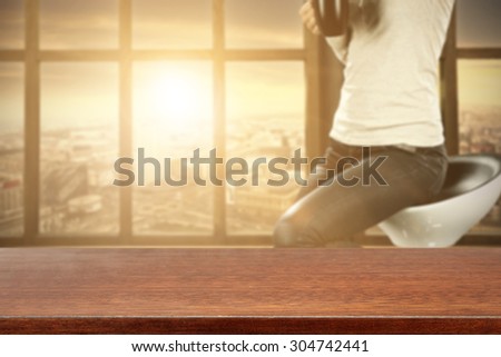 blurred background of big window with city landscape and dark brown desk top and woman on chair and sunlight