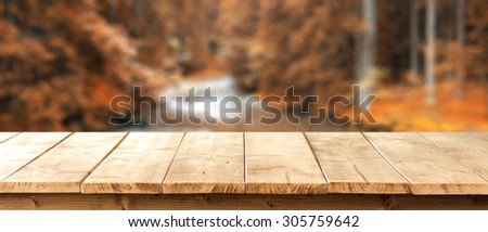blurred background of autumn forest with river and yellow wooden desk space and empty space for your decoration