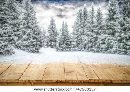 A table full of snowflakes with space for your product advertisement. Winter landscape of trees covered with snow and overcast with blue dramatic sky.