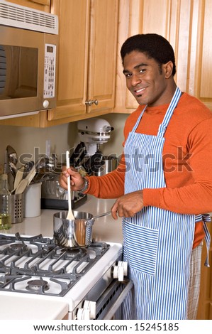 Handsome African-American man cooks dinner on stove in kitchen