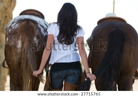 A young woman holds two horses by their tails