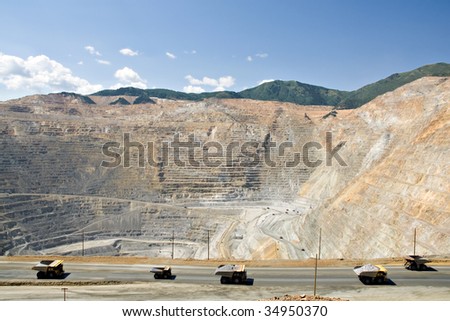 A line of monster dump trucks carry 250 ton loads of rock out of an open pit mine.