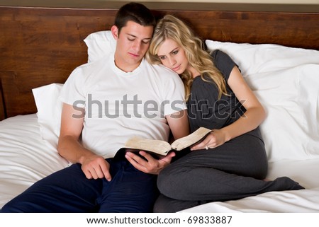 An attractive young couple read the Bible in bed