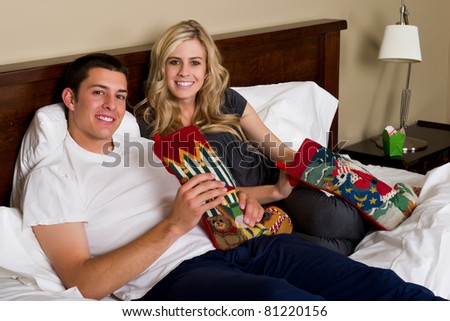 An attractive man and woman in their pajamas open gifts together in bed on Christmas morning