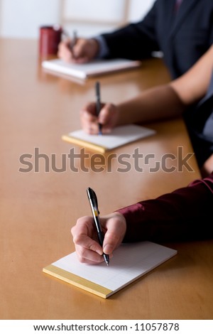 Business people taking notes at a meeting.  Shallow depth of field and no writing on paper.