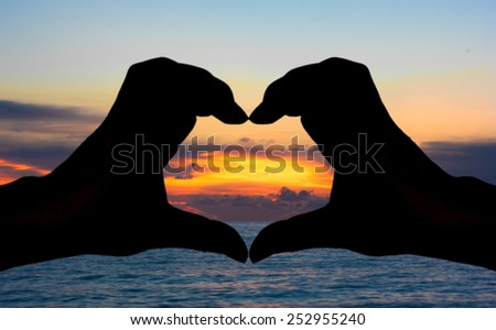 Silhouette of hand heart sign with sea and sunset background