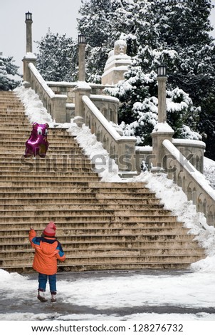A young girl holding a purple balloon, against the snow covered stairs.