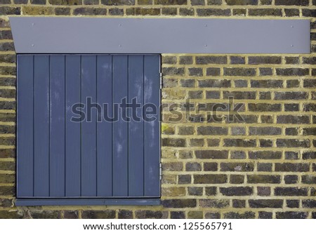 A colorful brick wall with a small pleasing slatted blue door in it and a clean blue/grey beam across the top