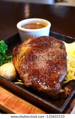Beef steak with vegetables, spaghetti and gravy. Being served on a hot pan