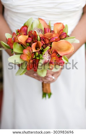 bride holding orange and red and green bouquet