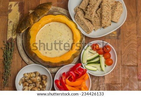 Cheese fondue in a roasted pumpkin with bread and assorted vegetables
