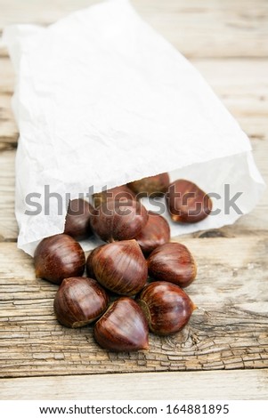 Fresh organic chestnuts in a white paper bag on wooden table
