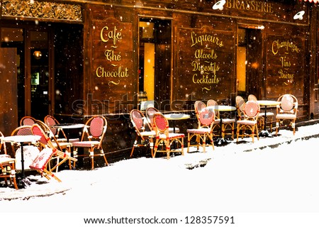 Classic old street brasserie in Paris viewed under the snowfall. Terrace circular tables and woven chairs are covered with fresh snow / Parisian cafÃ?Â© under the snowfall