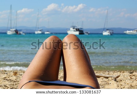 Legs and blue bikini beach view / Young women\'s wet and sun-tanned legs on the beach with the sea and ships view