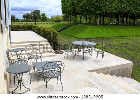 Open terrace with iron patio furniture and garden trees and lawn on the background, Gironde, France