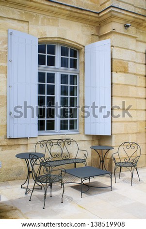 Open terrace with iron patio furniture and blue window shutters on the background, Gironde, France