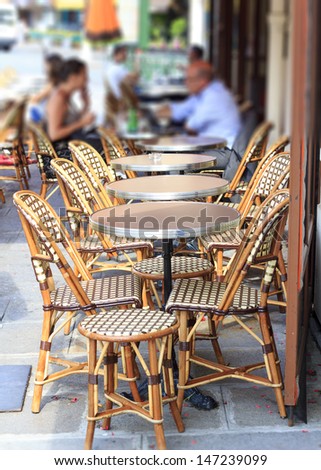 Open sidewalk cafe in Paris with traditional wicker cafe chairs and circular tables. Tilt shift