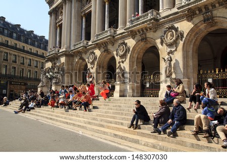 PARIS, FRANCE - APRIL 21 : People sitting at the steps of Paris Opera house while listening to the improvised concert of the street artists on April 21st 2013 in Paris, France