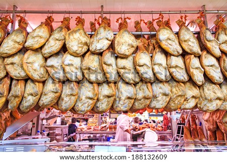 Large quantity ot Iberian hams hanging at Mercado Central - the central market of Valencia, Spain. Non-recognizable sellers in uniform in the background.