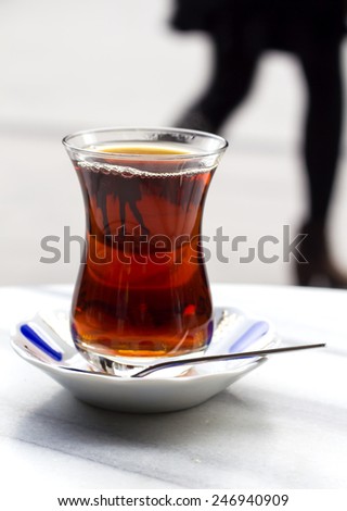 Traditional glass of turkish tea with the reflection and the background of the female legs coming from the girl passing by the terrace of the cafe in Istanbul, Turkey.