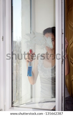 Young girl sits on a window sill and carefully washes and cleans a window