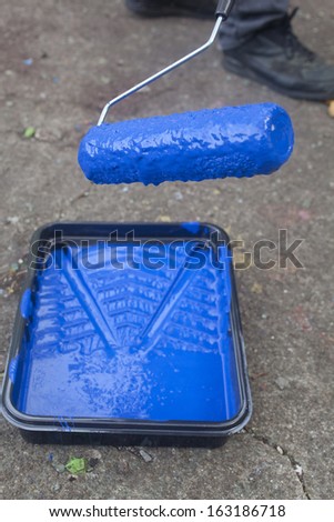 A paint roller dripping blue paint into a tray