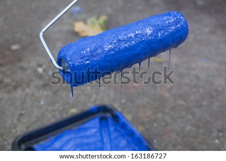 A paint roller dripping blue paint into a tray