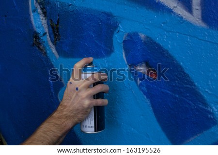 Graffiti artist holding a spray paint can to a wall