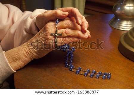 Elderly hands praying with Rosary Beads