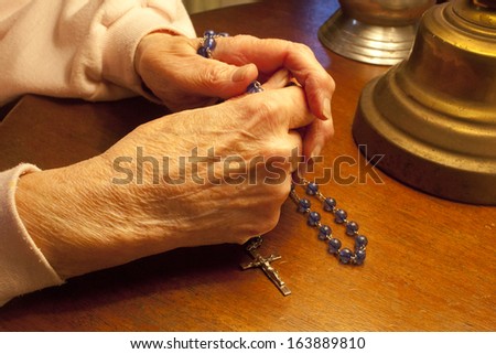 Elderly hands praying with Rosary Beads