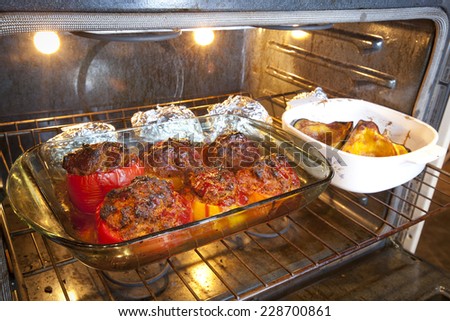 A dinner of stuffed bell peppers, winter squash and baked potatoes cooking in an oven.
