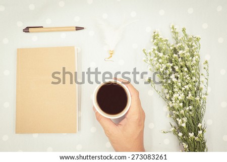 Hand with cup coffee and flower, book with retro filter effect