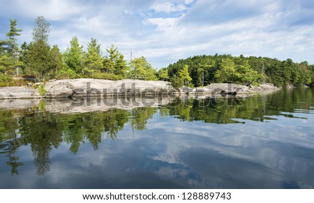 Reflection on a calm lake of a rocky shoreline on a northern lake